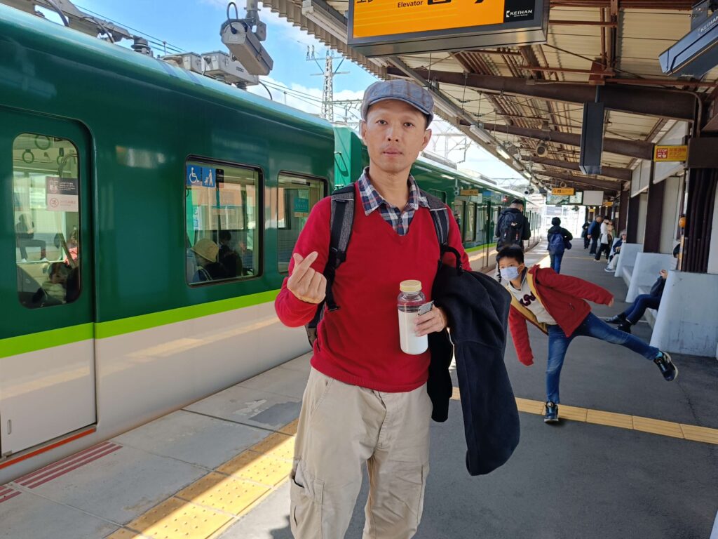 穿著紅衣的父子在京都六地蔵站月台與綠色京阪電車合照,慶祝行程回歸正軌