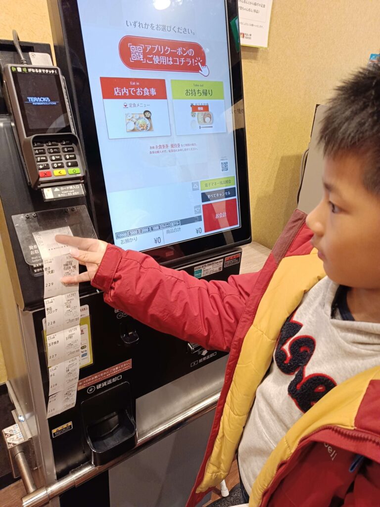 穿著紅色 mont-bell 外套的小男孩在日本大阪やよい軒自助點餐機前操作